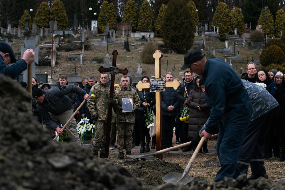 Men fill graves with dirt while soldiers and other mourners look on Tuesday in Lviv, Ukraine.