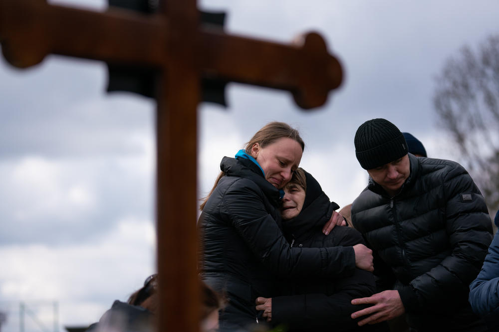 Ukrainian journalist-turned-soldier Viktor Dudar's mother (center) grieves at his grave as he's laid to rest Tuesday in Lviv, Ukraine.