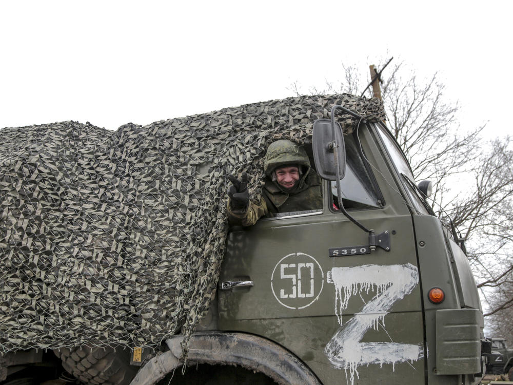 A serviceman waves from a military truck painted with the letter 
