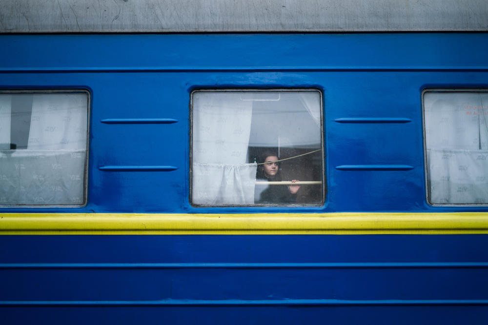A girl looks out the window of a train leaving the station in Lviv after waving farewell to her father.