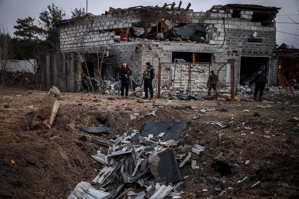<strong>March 12:</strong> Police officers and residents stand next to a shell crater in front of a house damaged by recent shelling, on the outskirts Kyiv.