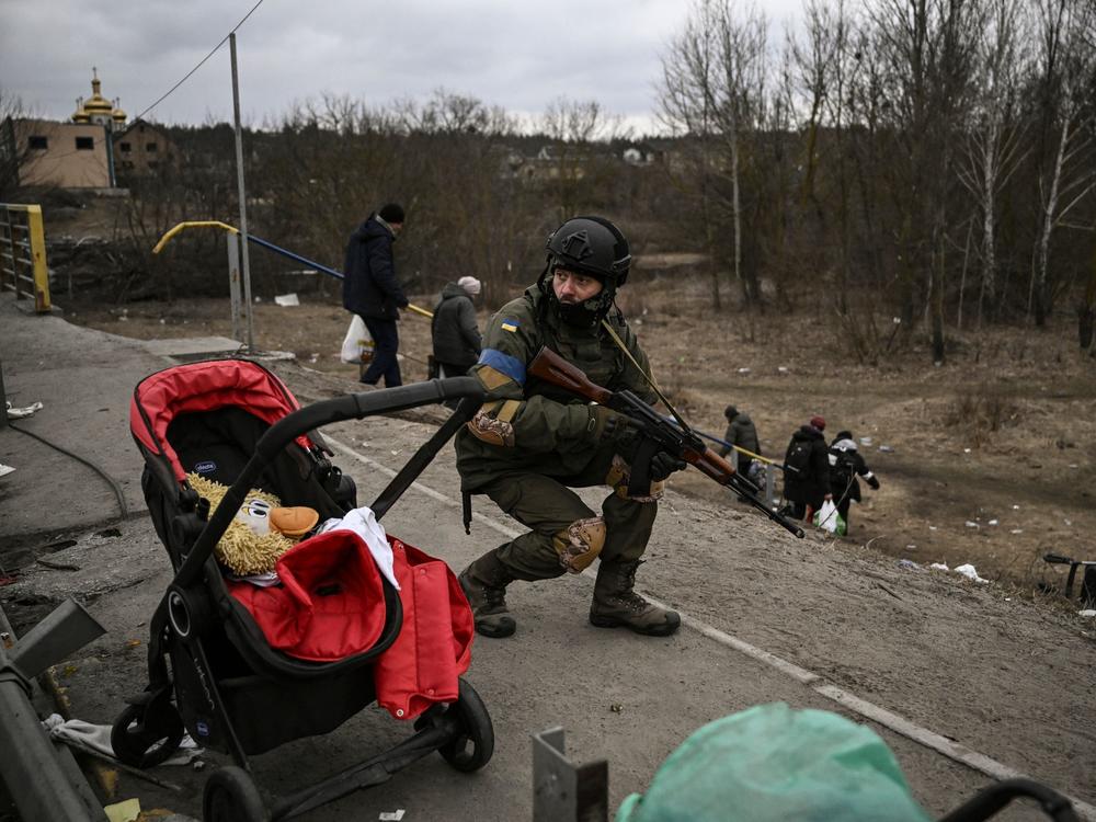 A Ukrainian serviceman takes cover as people evacuate the city of Irpin, near Kyiv, on Sunday.