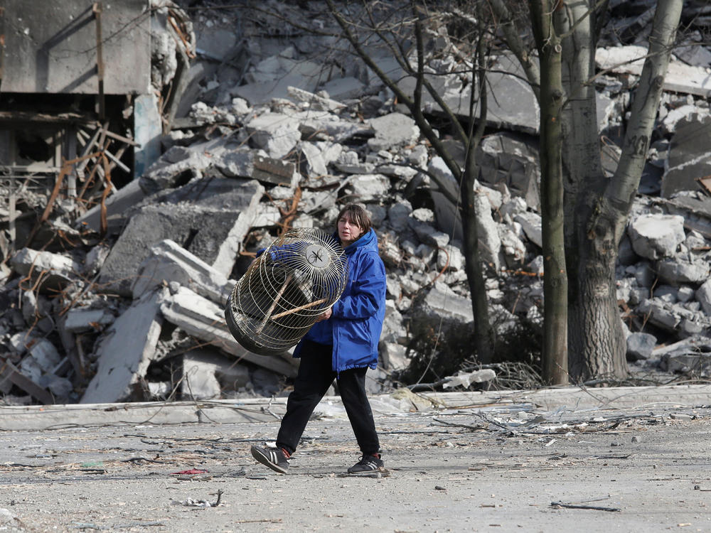 A local resident carries a cage on Thursday while walking past an apartment building destroyed in the besieged city of Mariupol.