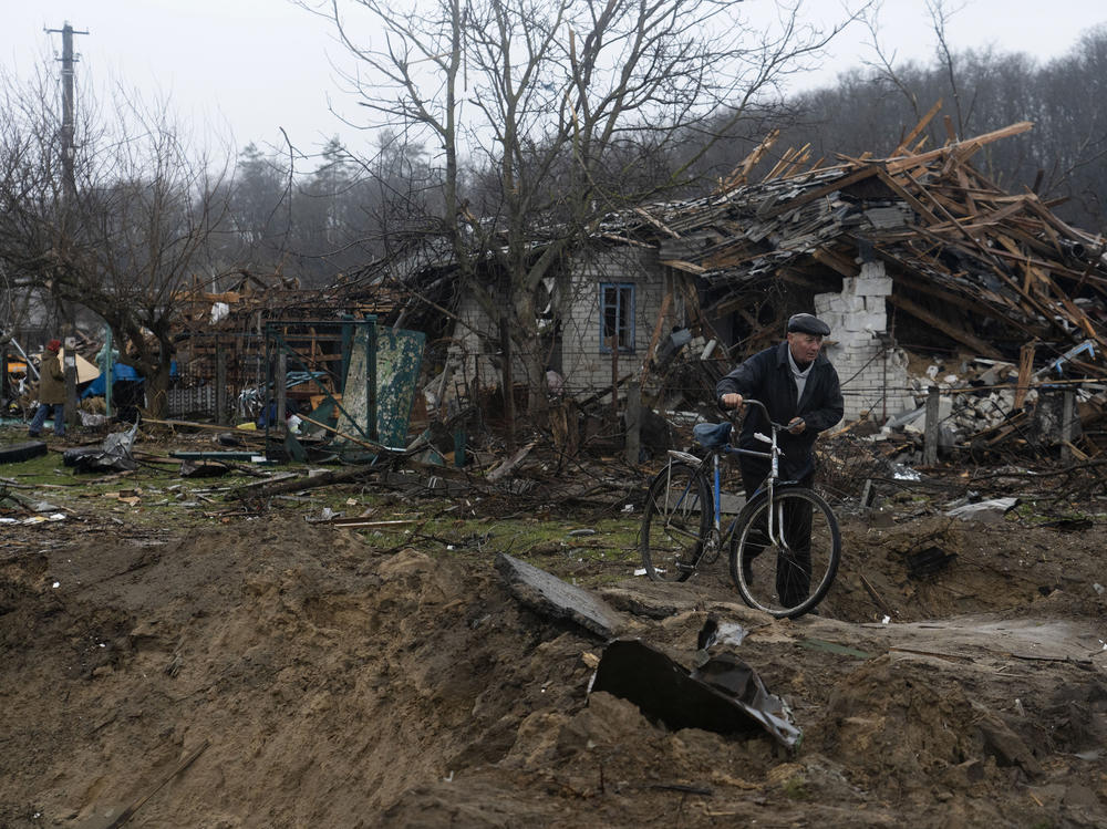 A resident walks his bicycle on a narrow path between craters made by artillery in a neighborhood of Chernihiv.