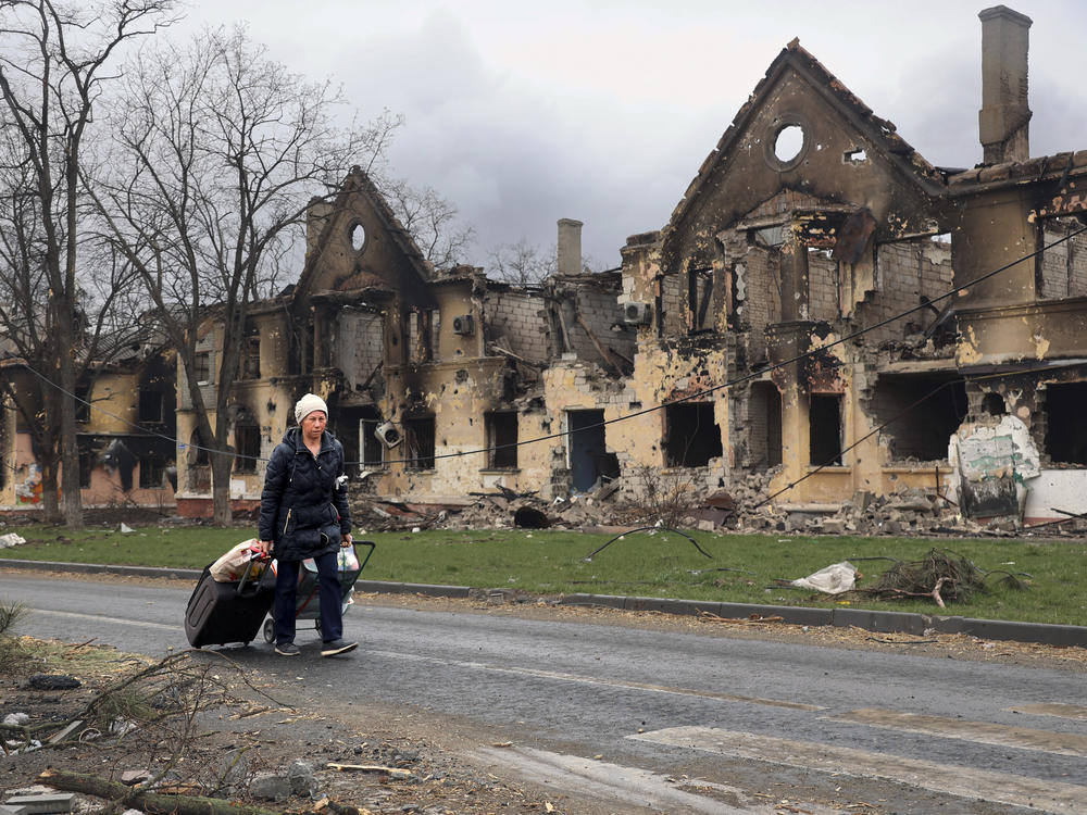 A woman on April 8 pulls her baggage past houses damaged during fighting in Mariupol, Ukraine.
