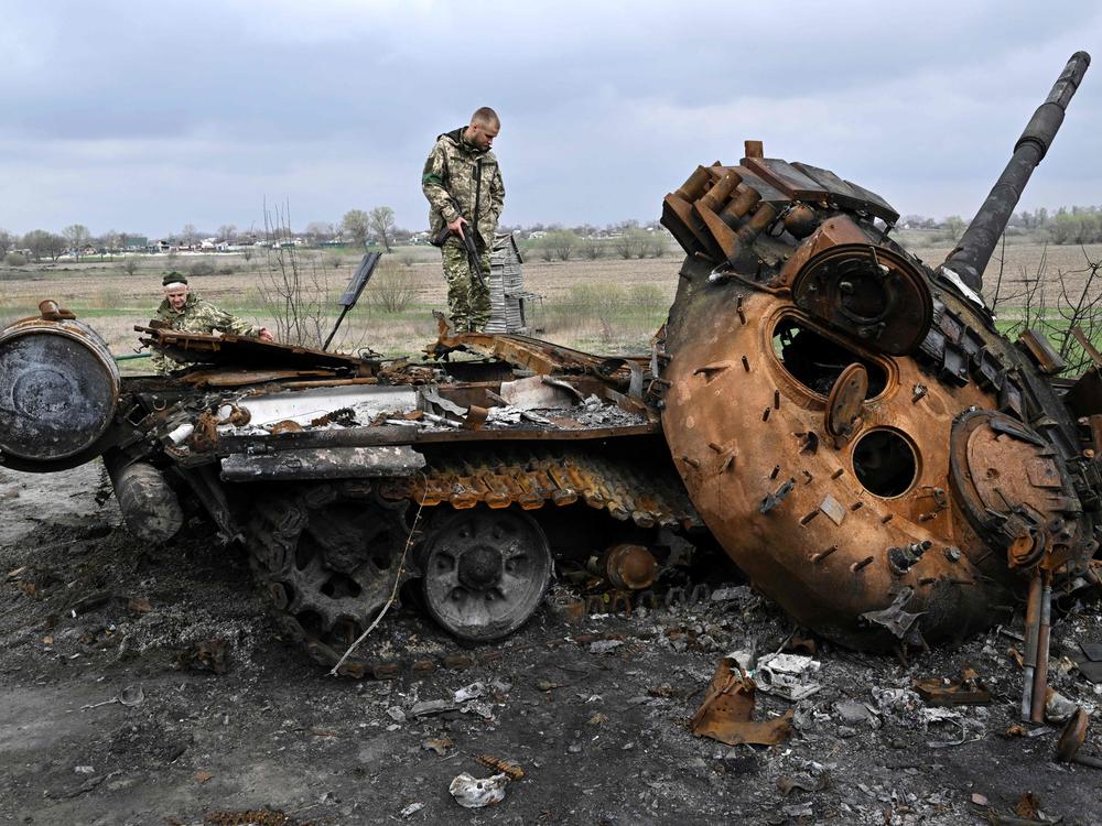 Ukrainian servicemen look at a destroyed Russian tank on a road in the village of Rusaniv, in the Kyiv region on April 16, 2022.
