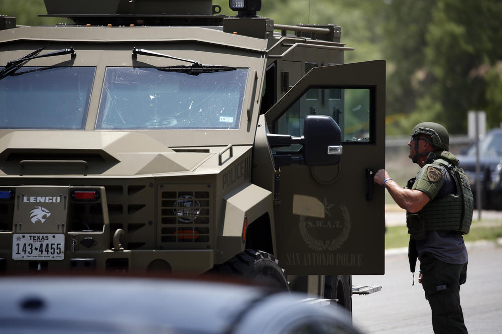 Law enforcement personnel stand next to an armored vehicle.