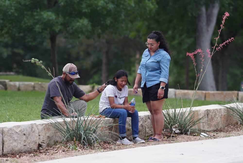 A girl cries, comforted by two adults, outside the Willie de Leon Civic Center where grief counseling will be offered in Uvalde, Texas.