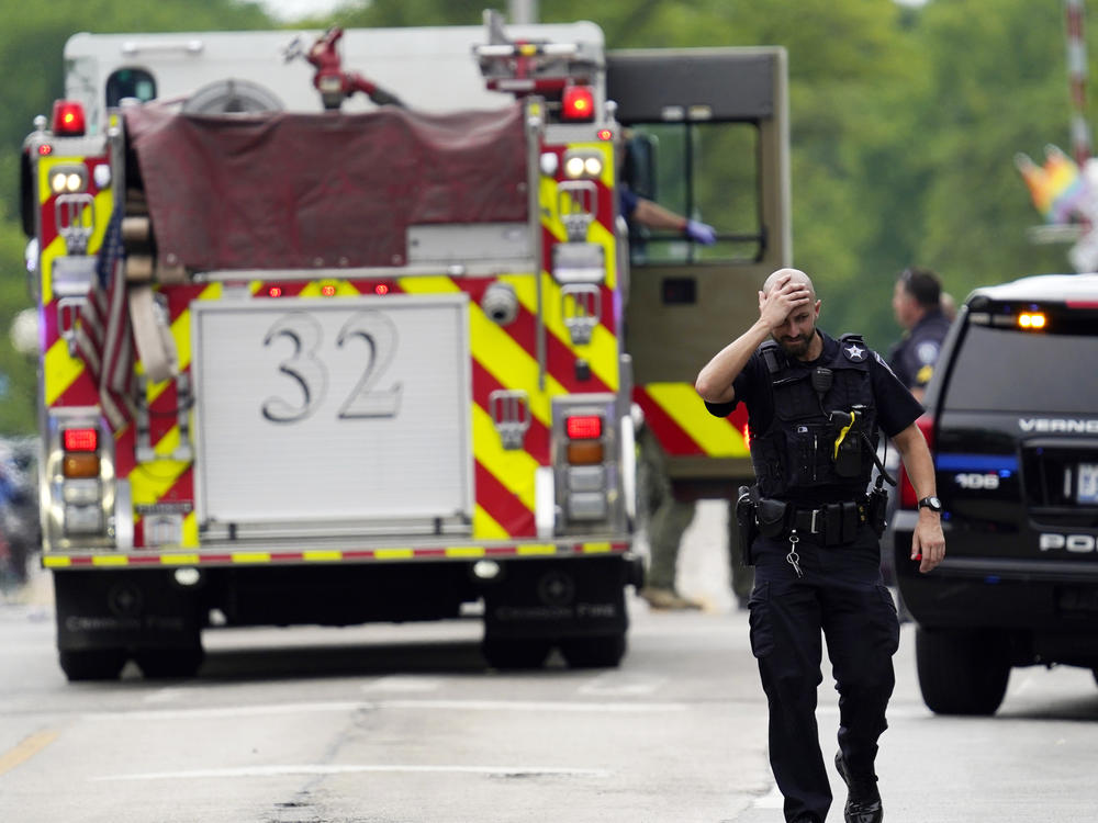 A police officer reacts as he walks in downtown Highland Park, Ill., a suburb of Chicago, Monday, as law enforcement continues a search for the suspected gunman who killed at least six.