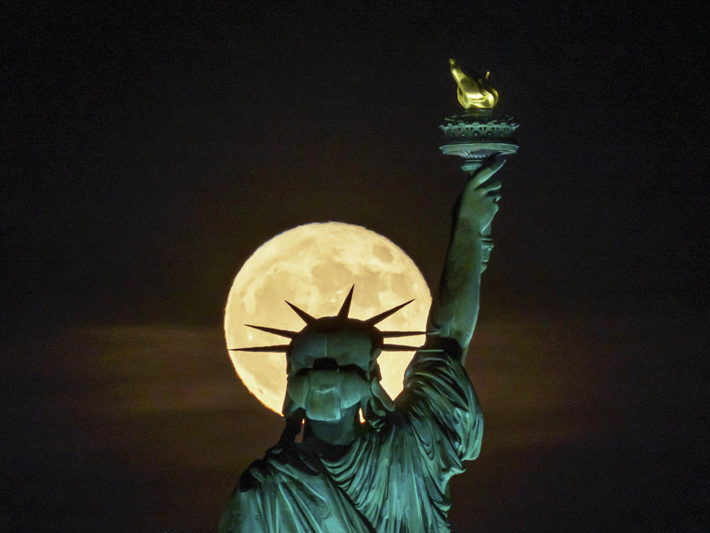 The strawberry supermoon rises in front of the Statue of Liberty in New York on June 14. After July's supermoon on Tuesday there will be one more for the year on Aug. 11.