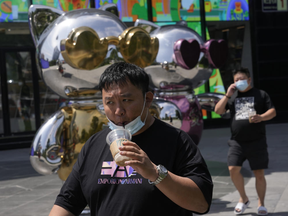 A man lowers his mask to drink from a cup as he past near a mall, Wednesday, July 13, 2022, in Beijing.