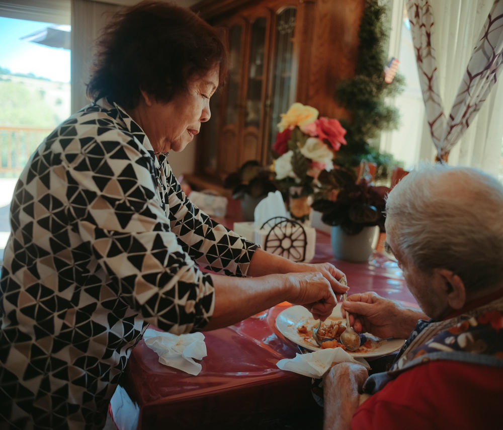 A resident manages his plate with a little help from Angelita Perez, the owner of Hillcrest Care, a small assisted-living facility in El Dorado Hills, Calif., on July 14, 2022.