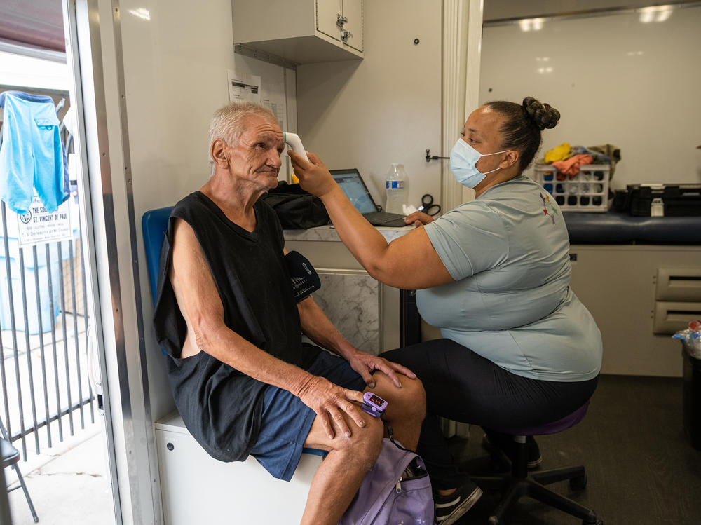 Alicia Williams checks the vital signs of Paul Yager inside the mobile medical unit parked outside St. Vincent de Paul, a charitable organization with a soup kitchen in Phoenix's Sunnyslope neighborhood, on Aug. 9. Yager, 64, is unsheltered, lives with preexisting conditions and has been waiting for housing assistance for two years.
