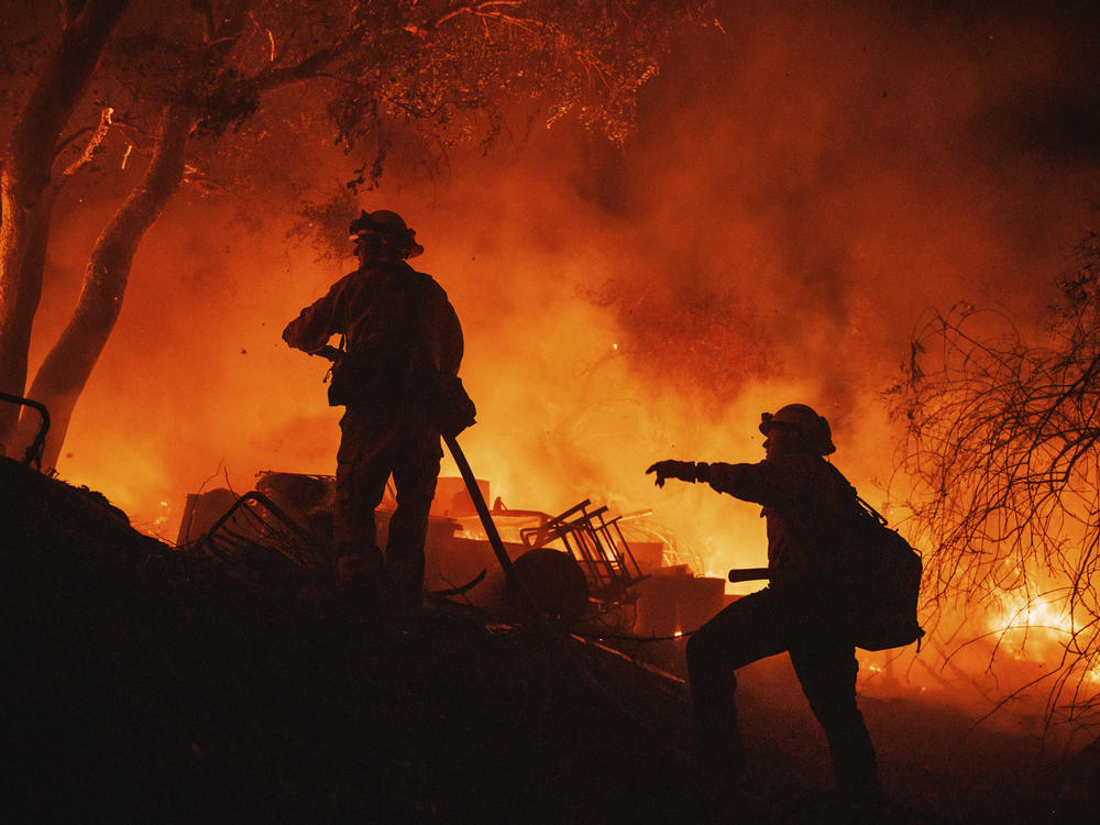 Firefighters coordinate efforts at a burning property while battling the Fairview Fire on Monday, near Hemet, Calif.