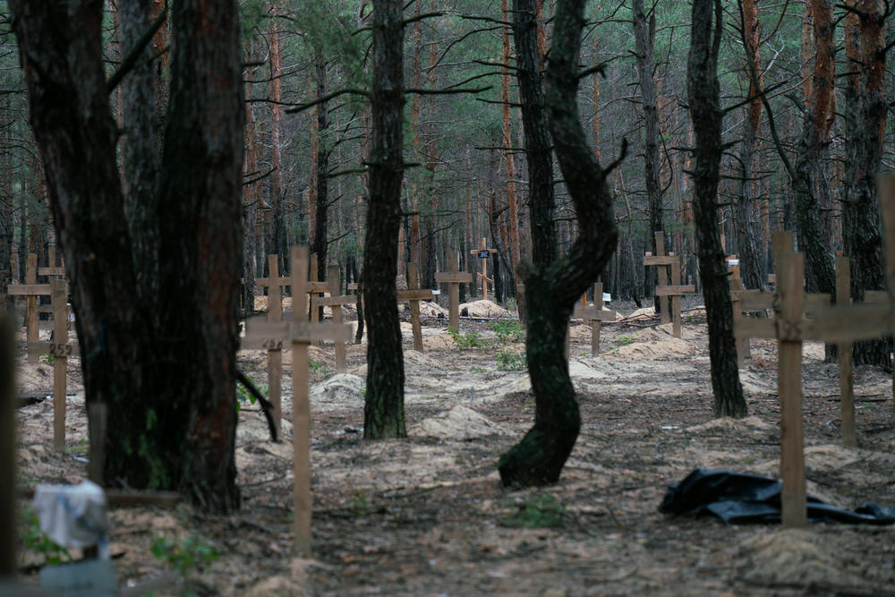 Wooden crosses mark burials at a mass grave site in newly liberated Izium, Ukraine. Some of the graves have a name and date written in thick black marker, others have simply a number scrawled across — unidentified.