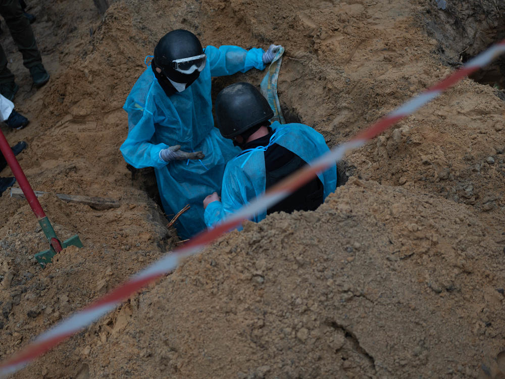Ukrainian investigators exhume bodies from a mass grave site in Izium on Friday.