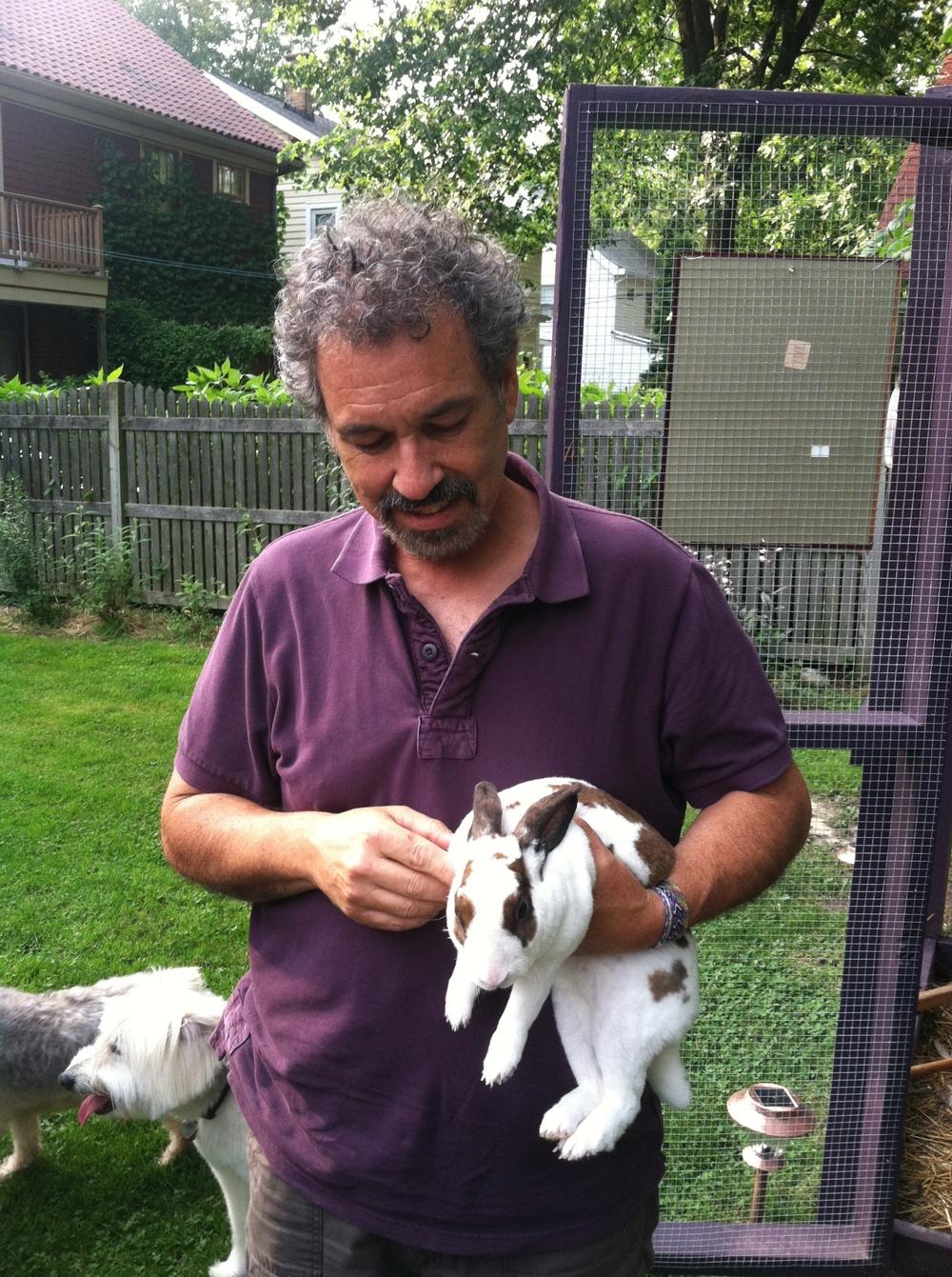 Ken holds his rescue rabbit, Owen, in his backyard. Two of his rescue dogs are behind him.