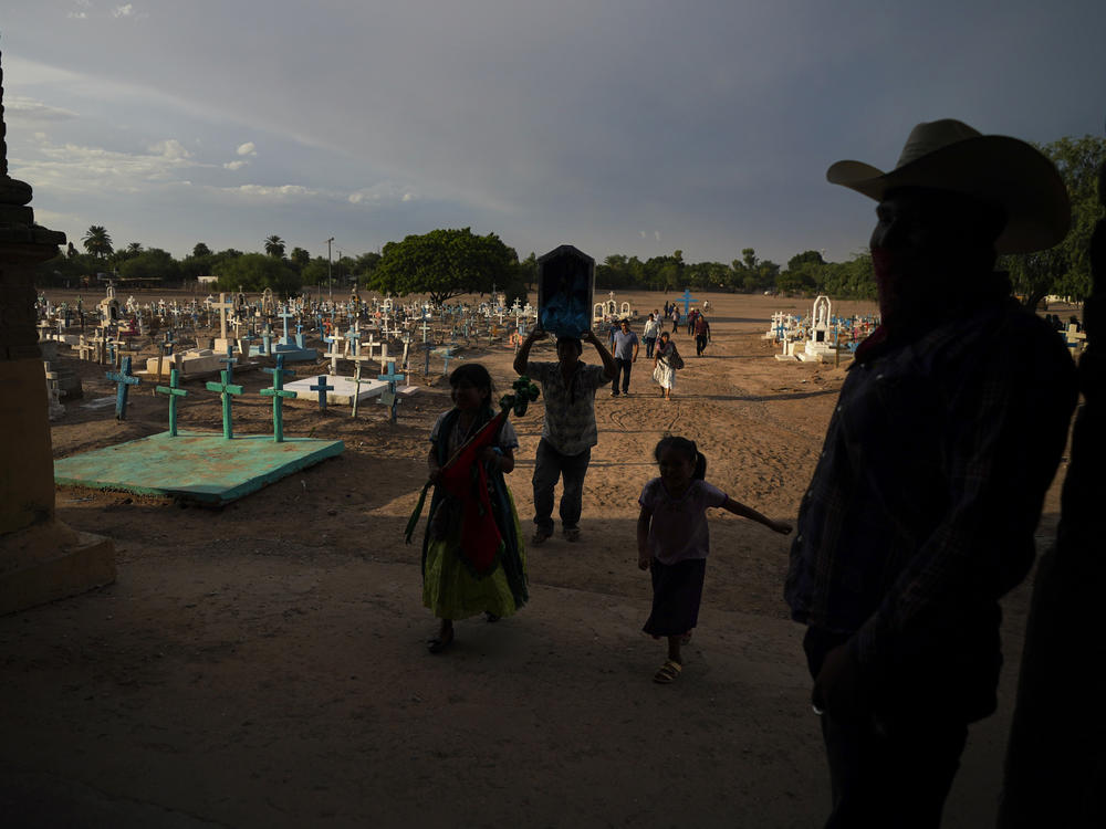 A Yaqui Indigenous family walks past the cemetery where slain water-defense leader Tomás Rojo is buried, outside a church where they arrive to celebrate the Virgin Mary in Potam, Mexico, Tuesday, Sept. 27, 2022.