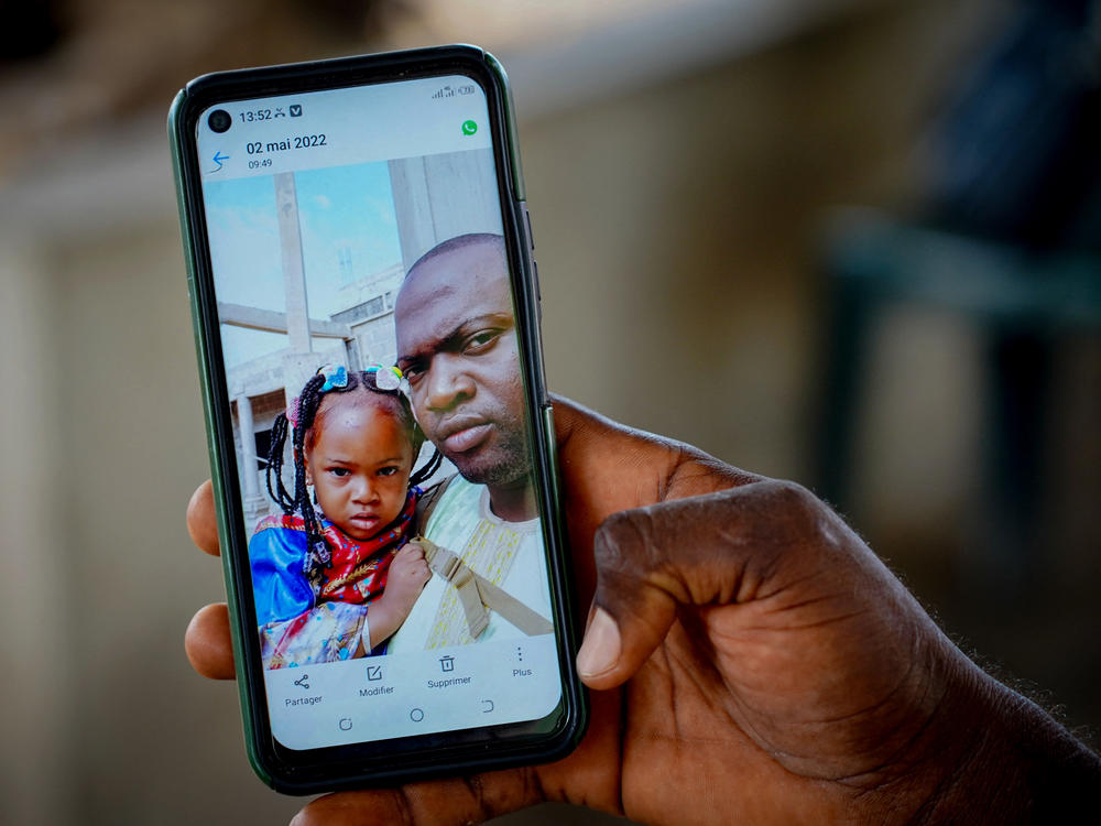 Wuri Bailo Keita, 33, holds a mobile phone showing a picture of himself and his late daughter, Fatoumatta, who is believed to have died of acute kidney failure after ingesting contaminated cough syrup manufactured in India. The family lives in Banjul,  Gambia. The photo is from October 10.