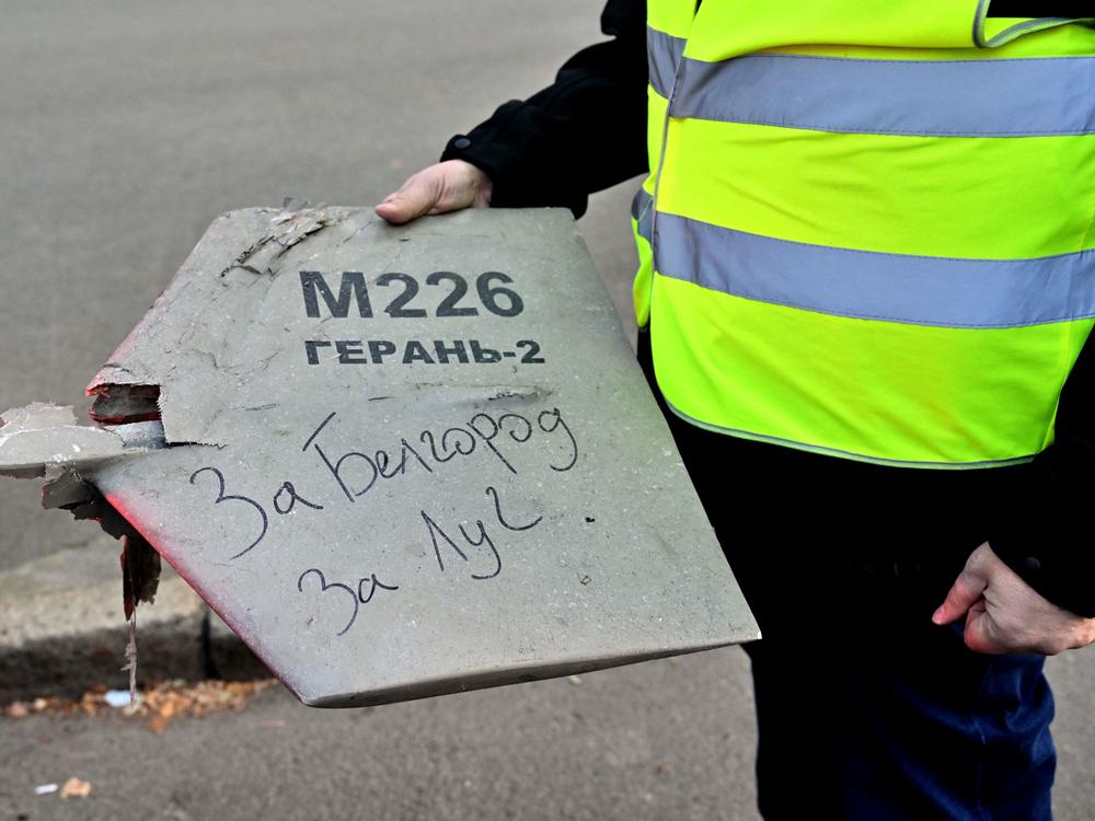 A police expert holds a fragment of a drone with a handwritten inscription reading 