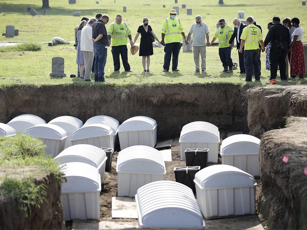 A group prays during a small ceremony as remains from a mass grave are re-interred at Oaklawn Cemetery on July 30, 2021, in Tulsa, Okla.