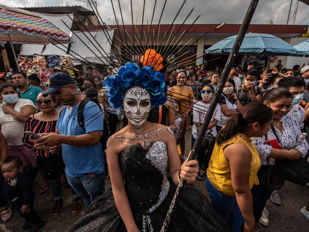 Una joven vestida con maquillaje de Santa Muerte espera afuera del panteón con algunos participantes