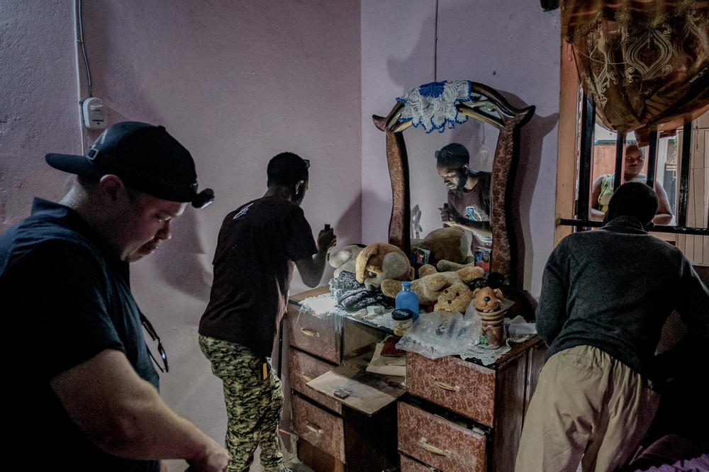 Baldé and Keita search behind a chest of drawers for a snake that had been reported at a home in Kindia as family members watch through the window. A large forest cobra was found moments later.