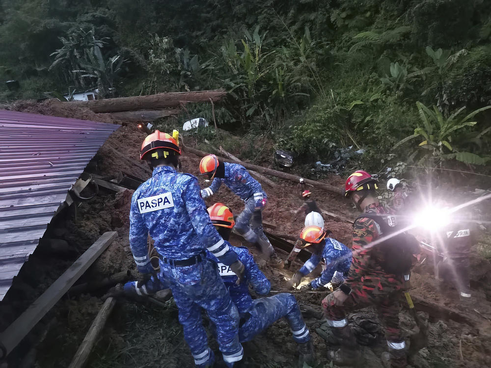 In this photo provided by Civil Defense Department, Civil Defense personnel search for survivors buried after a landslide hit a campsite in Batang Kali, Malaysia, on Friday.