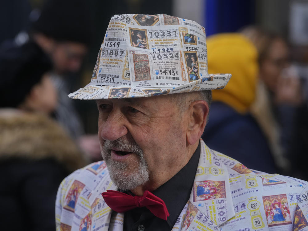 A man with a suit and hat decorated in printed lottery tickets stands outside the famous Doña Manolita lottery ticket shop in downtown Madrid, Spain, Wednesday, Dec. 21, 2022.