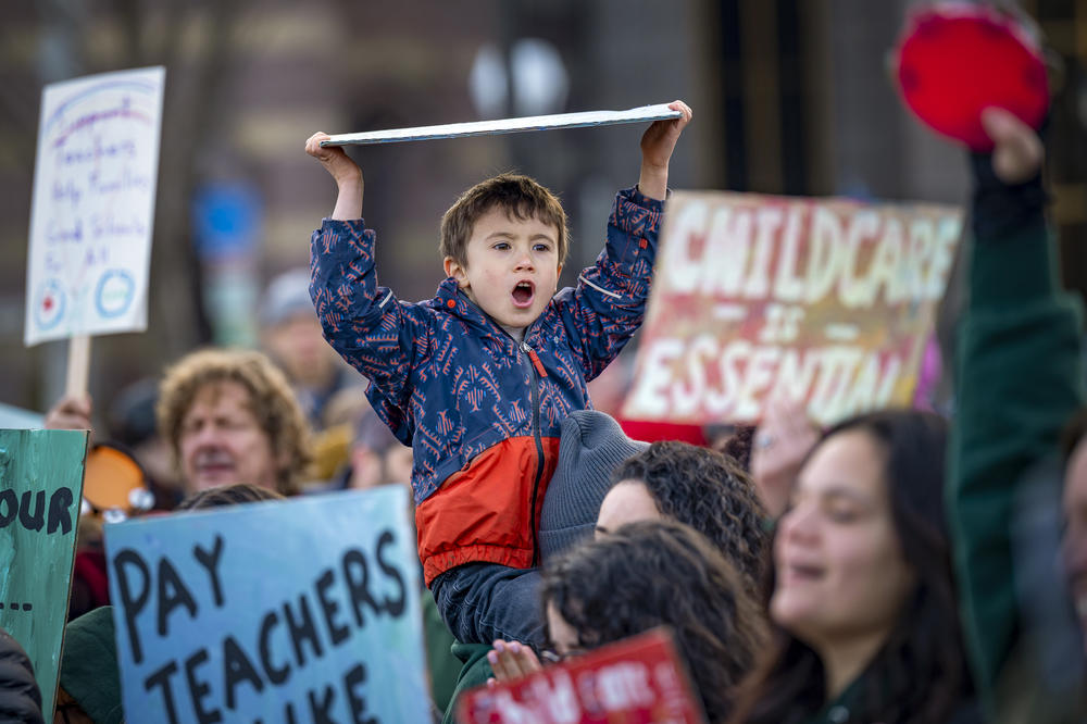 5 year old Joaquin Freiberg cheers above the crowd, hoisting a sign which reads, 