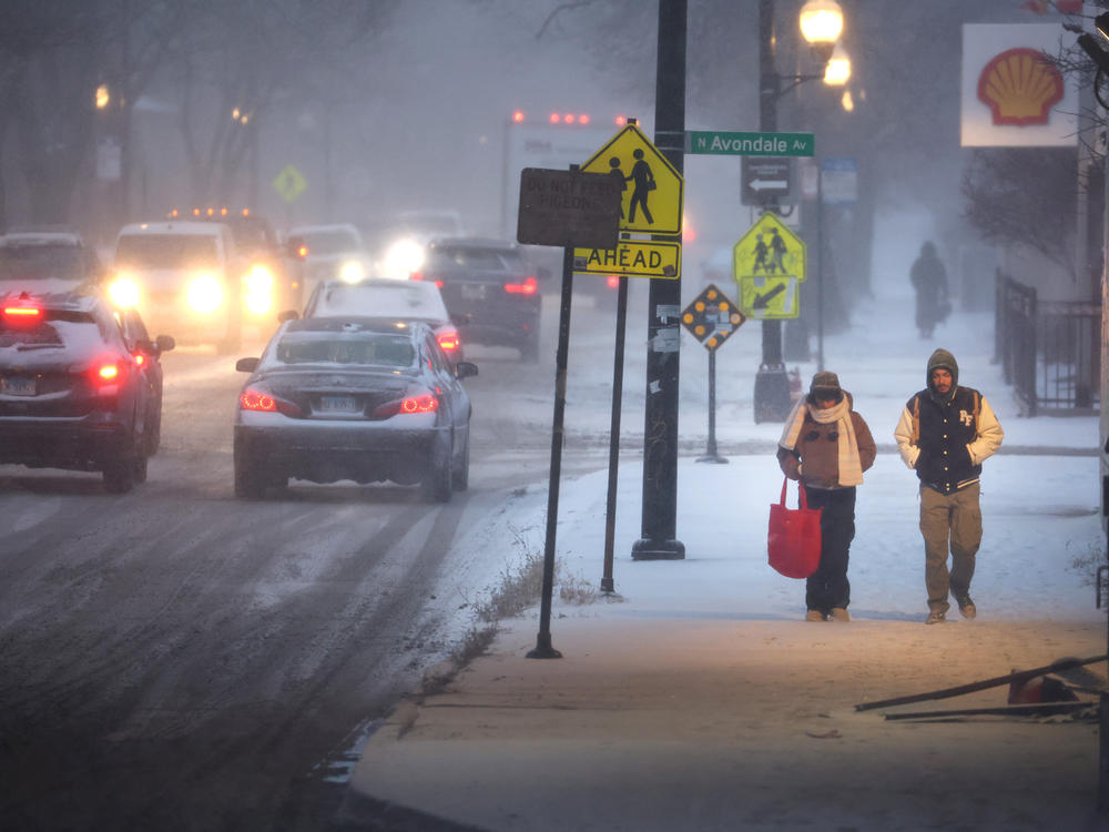 Pedestrians navigate a snow-covered sidewalk in Chicago, on Thursday. Severe winter weather has impacted tens of millions of people in the U.S.