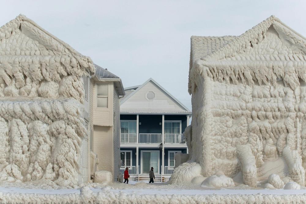 People walk between frozen homes in the waterfront community of Crystal Beach in Fort Erie, Ontario, Canada.