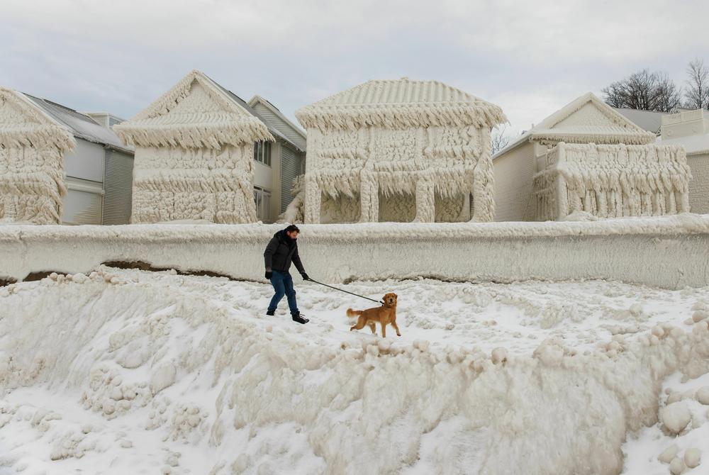 A person and dog walk by homes covered in ice at the waterfront community of Crystal Beach in Fort Erie, Ontario, Canada.