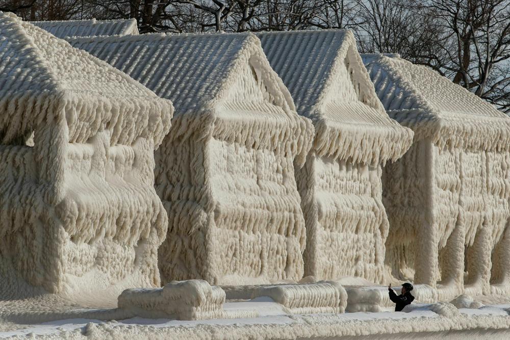 A person takes photos of a scene of frozen houses in the waterfront community of Crystal Beach in Fort Erie, Ontario, Canada.