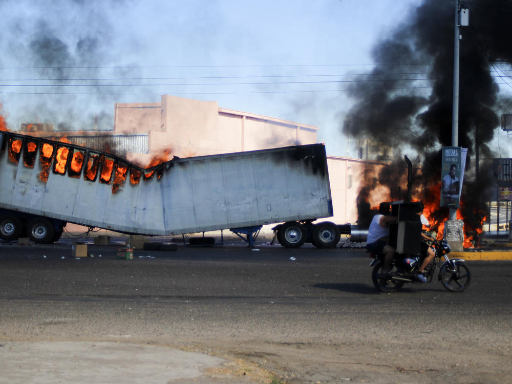 Men ride on a motorcycle past a burning truck on the streets of Culiacan, Sinaloa state, Thursday, Jan. 5, 2023. Mexican security forces have captured Ovidio Guzmán, an alleged drug trafficker wanted by the United States and one of the sons of former Sinaloa cartel boss Joaquín 