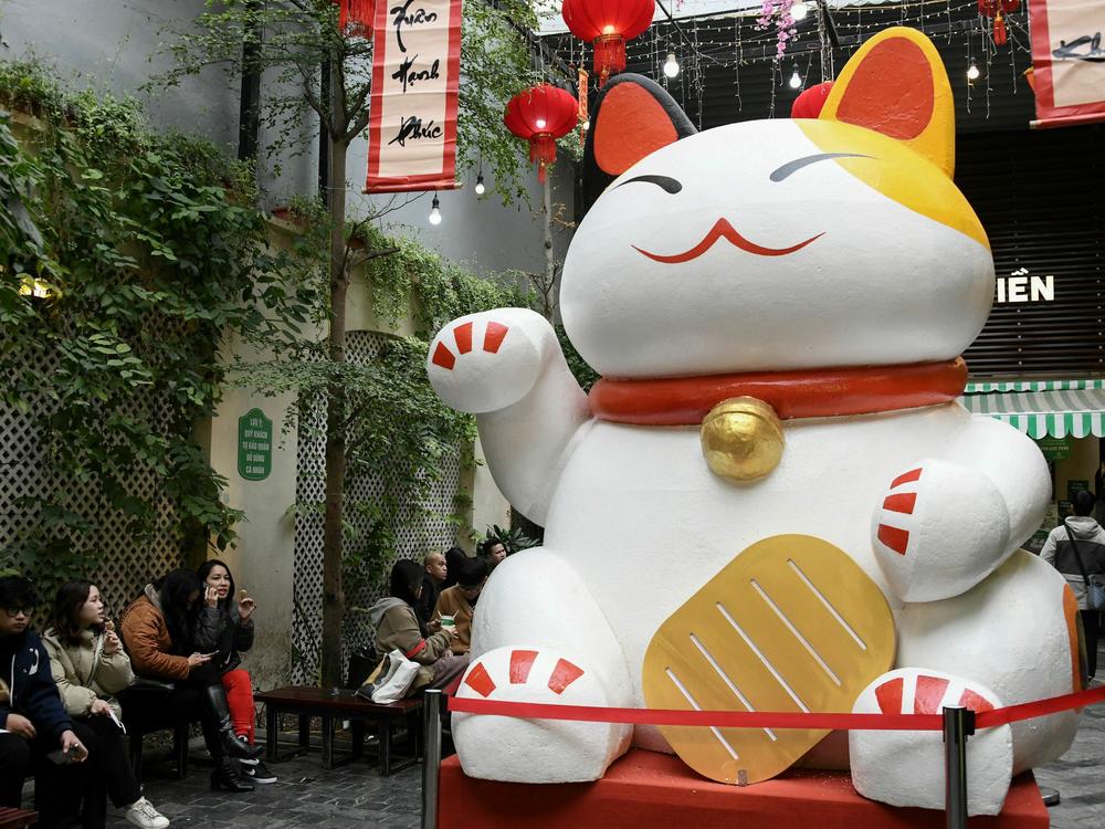 People eat ice cream next to a large cat statue at a shop in Hanoi this week. Cat statues of all sizes and styles line the streets of Vietnam ahead of the Lunar New Year.