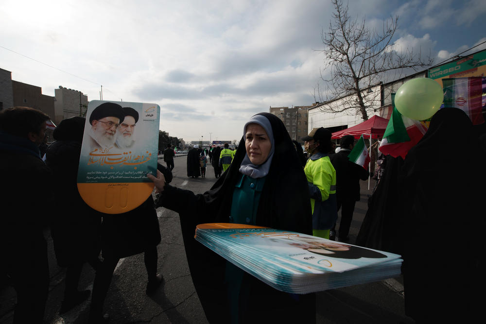 A woman distributes placards with the images of Ali Khamenei (r) Iran's current Supreme Leader, and Ayatollah Khomeini, the country's first Supreme Leader, during the 44th anniversary of the revolution celebrations, in Tehran. The placard quotes Khamenei saying 