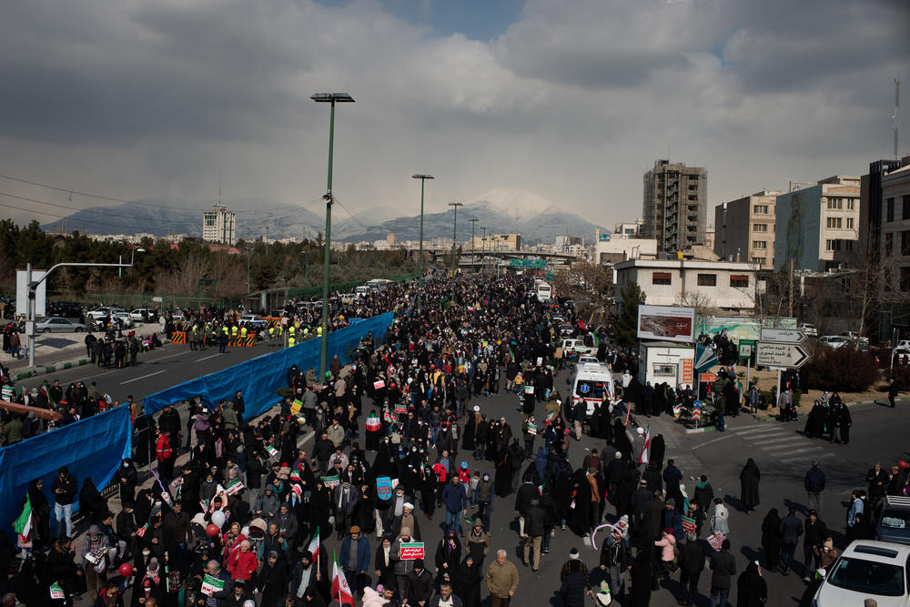 The crowd parades through the western part of Tehran, the Alborz mountain range in the distance.