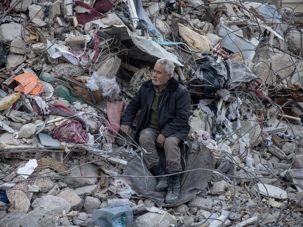 A man watches a search and rescue operation from a pile of rubble in Hatay, Turkey, after the earthquake.