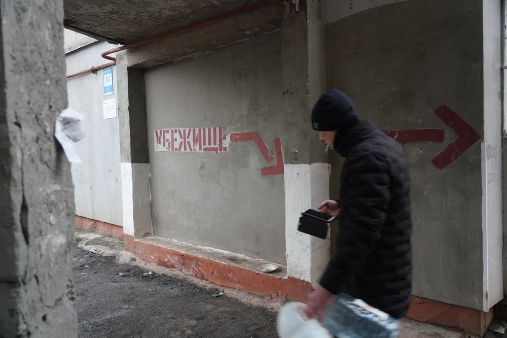 A man walking on the east side of Mariupol, by a sign, in Russian, that read Ubezhishe, meaning bomb shelter.