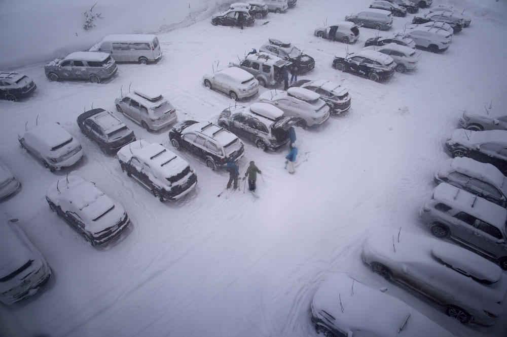 People stand in the parking area of the Alpine Base Area at Palisades Tahoe during a winter storm on Friday in Alpine Meadows, Calif.