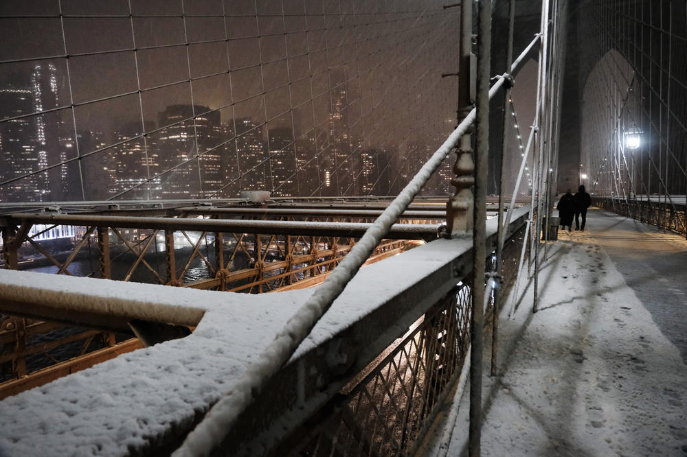 Snow falls as people walk across the Brooklyn Bridge on Monday in New York City.