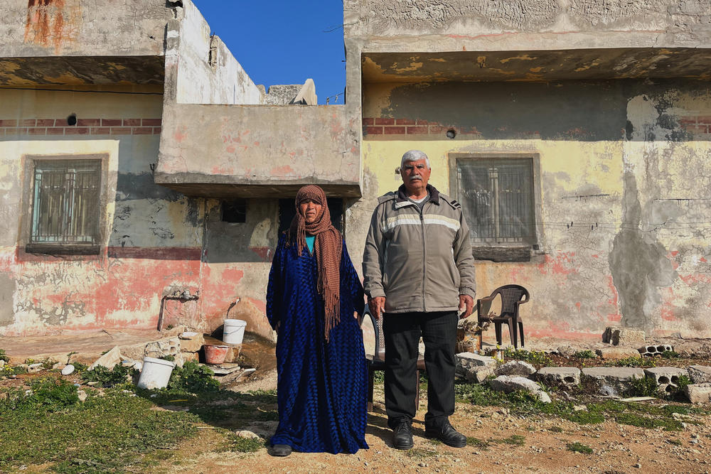 Jassem al-Hussein and his wife Dahiya, in their 60s, stand in front of the home they share with their divorced daughter and their 8-year-old grandson. Al-Hussein has had multiple surgeries, is unemployed and says his two sons left Syria during the war and live as refugees in Lebanon.