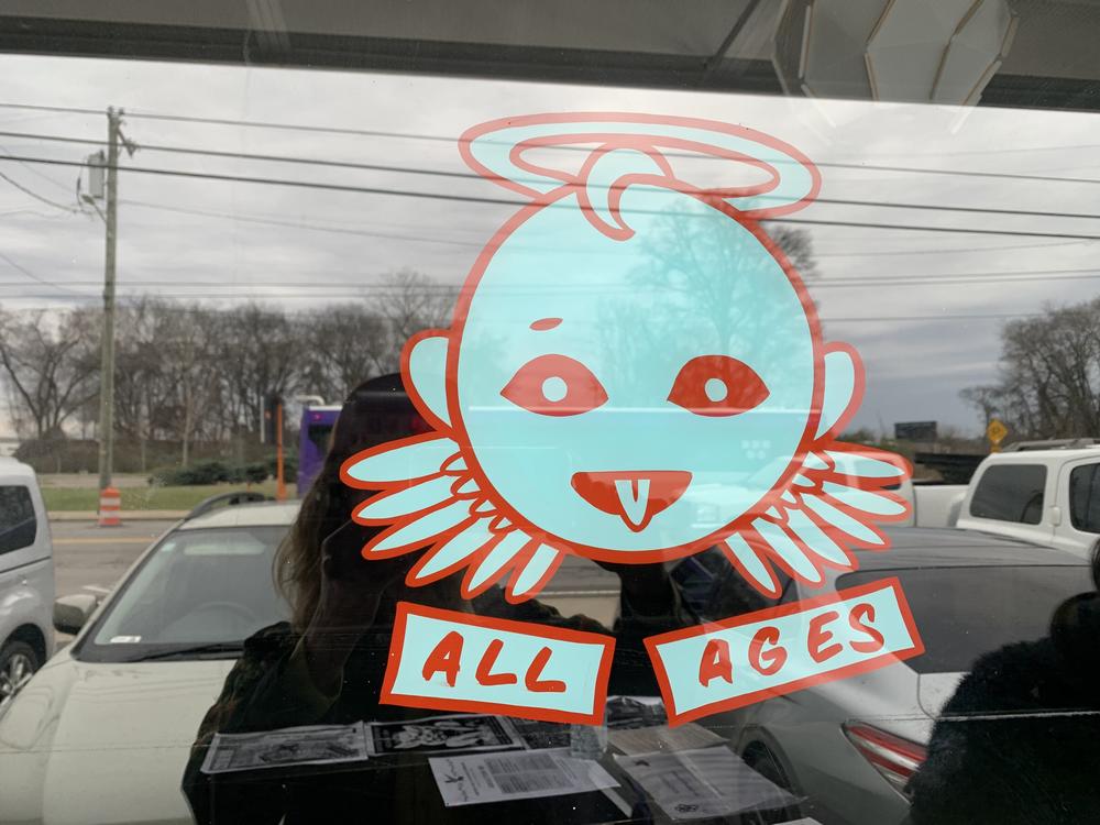 Adhered to the window of Drkmttr Collective's storefront is a sticker of a cartoon angel beaming goofily over the words 