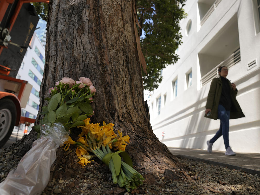 A woman on Wednesday walks past flowers left outside an apartment building in in San Francisco where technology executive Bob Lee was fatally stabbed.