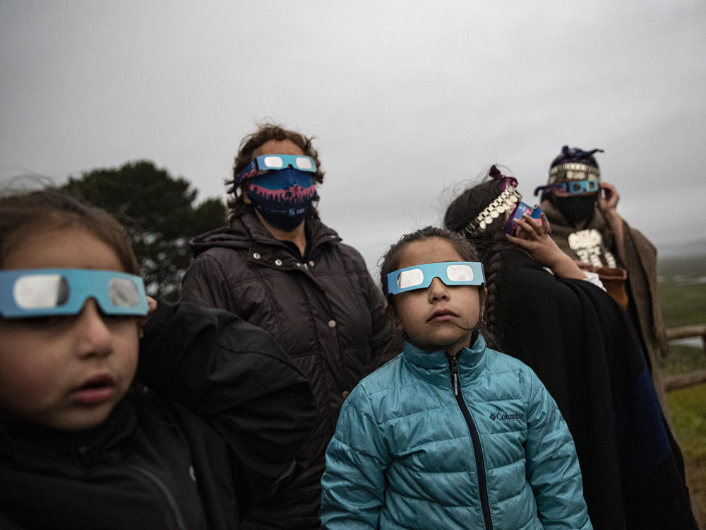 A Mapuche Indigenous family uses special glasses to try and observe a total solar eclipse in Carahue, La Araucania, Chile, Monday, Dec. 14, 2020. The total eclipse was barely visible from Carahue because of an overcast sky.