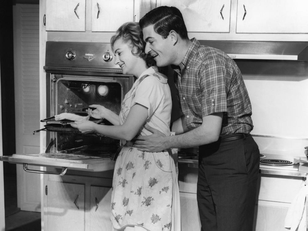 UNITED STATES - CIRCA 1950s: Couple in kitchen. Women in opposite-sex marriages may be contributing more to their families' income, but they're also still shouldering more of the workload at home, according to a new report.