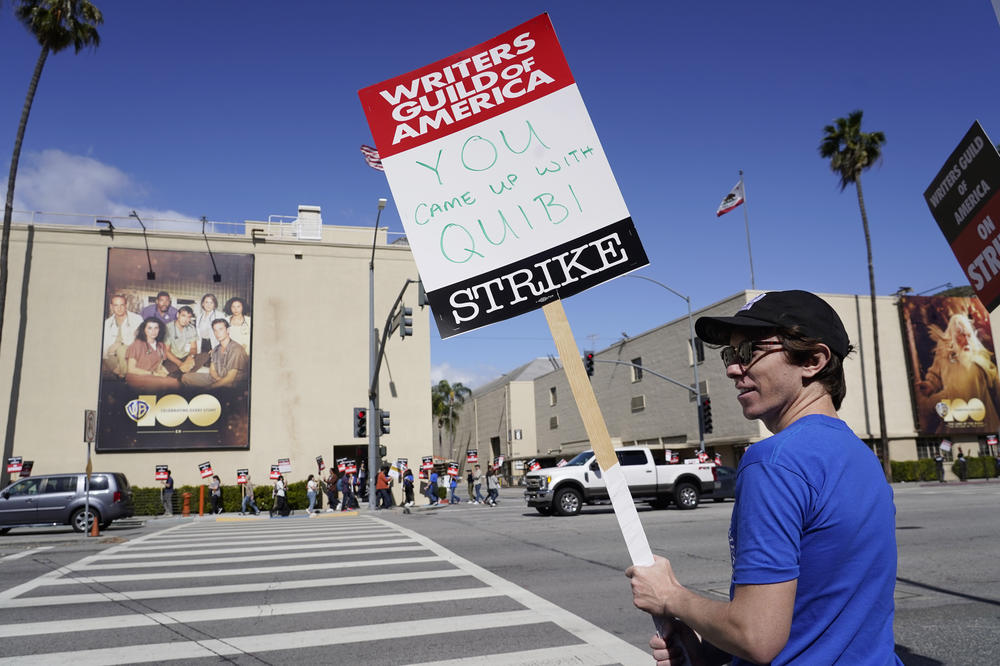 Writer Jono Matt holds a sign referring to the short-lived streaming service Quibi at the WGA picket line outside Warner Bros. Studios in Burbank.