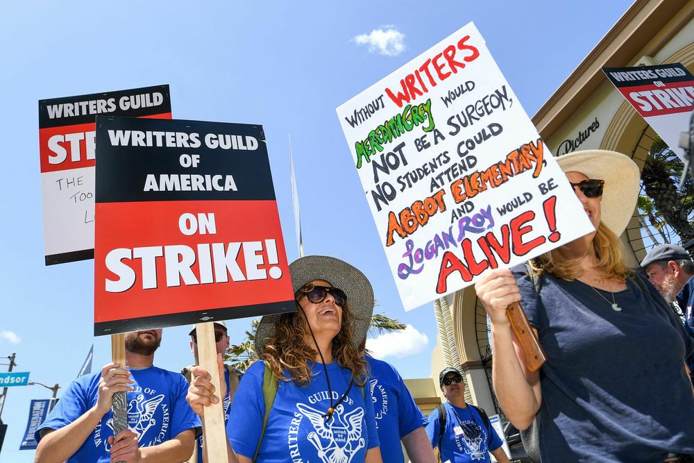 A picketer at Paramount Studios in Los Angeles carries a sign with references to the television shows <em>Grey's Anatomy, Abbott Elementary</em> and <em>Succession</em>.