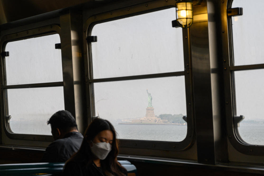 A passenger wearing a face mask rides the Staten Island Ferry past the Statue of Liberty during heavy smog in New York on June 6, 2023.